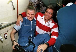 Astronaut Shannon Lucid (holding a camera) is greeted by her replacement, astronaut John Blaha in the docking module (DM) attached to the Mir space station. 